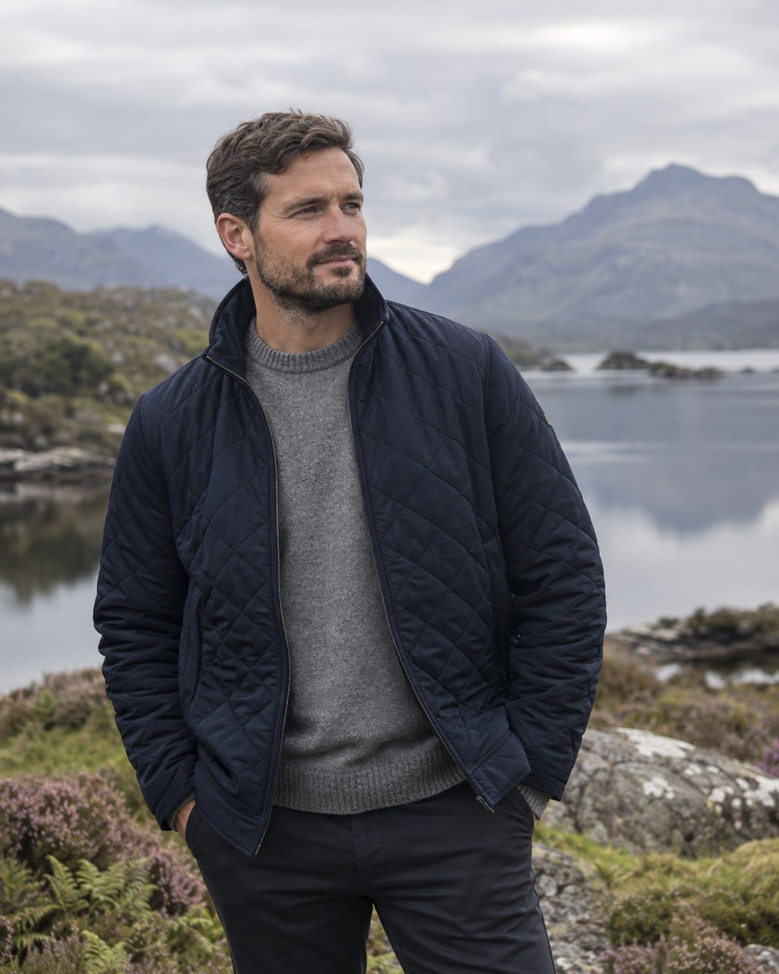 A man in a navy quilted jacket over a grey jumper standing by a lake in Connemara.