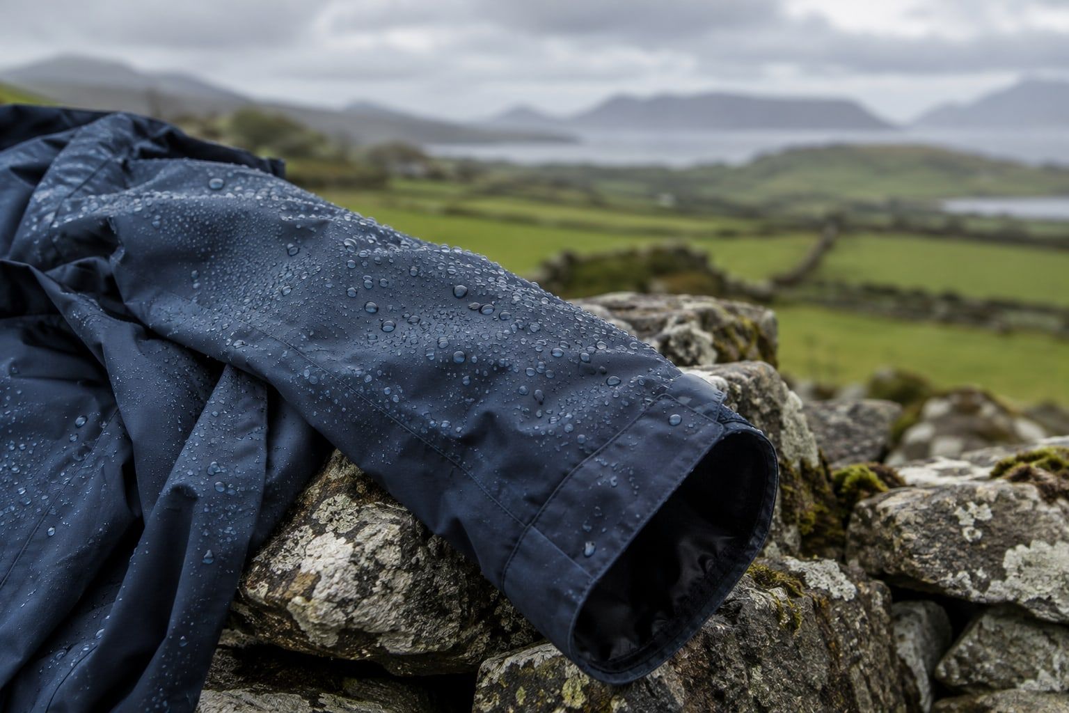 Rain beading on the sleeve of a navy waterproof jacket draped over a dry-stone wall.